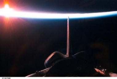 The sun illuminates the Earth's atmosphere during a sunrise, seen from the Space Shuttle Discovery after departure from the International Space Station on Saturday, Aug. 6, 2005. A portion of the shuttle's aft cargo bay, its vertical stabilizer and orbital maneuvering system (OMS) pods are seen in the foreground.